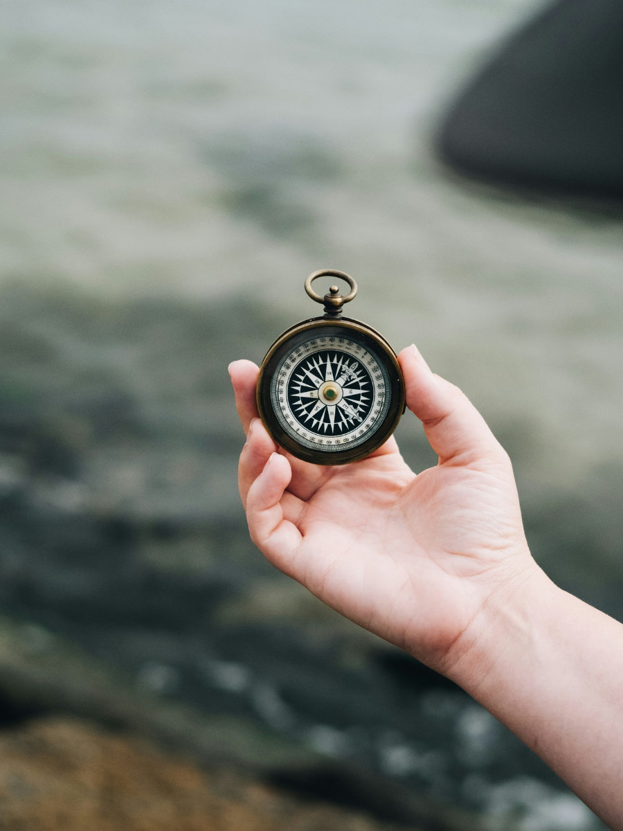 hand holding a compass by the ocean