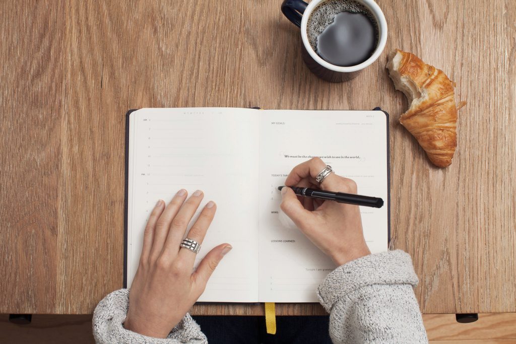 woman writing in journal with coffee and a croissant - find your writing motivation